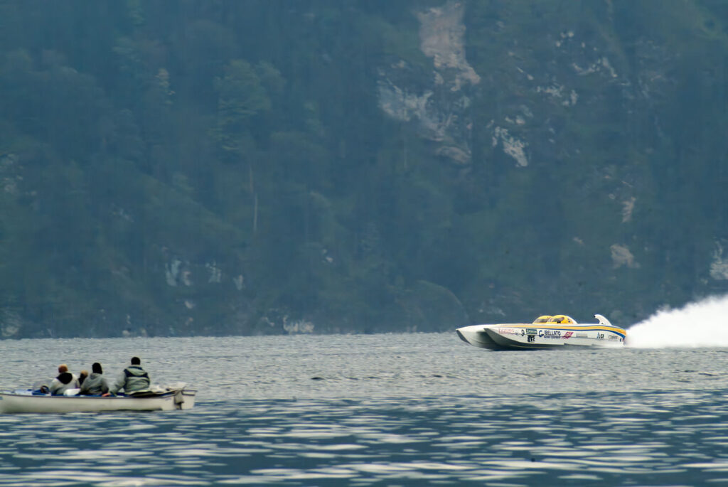 Mehrere Personen in einem Ruderboot betrachten ein Rennboot.
