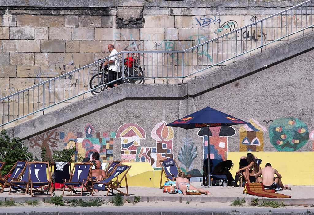 Ein Abgang zum Donaukanal, davor einer Gruppe Personen in Liegestühlen