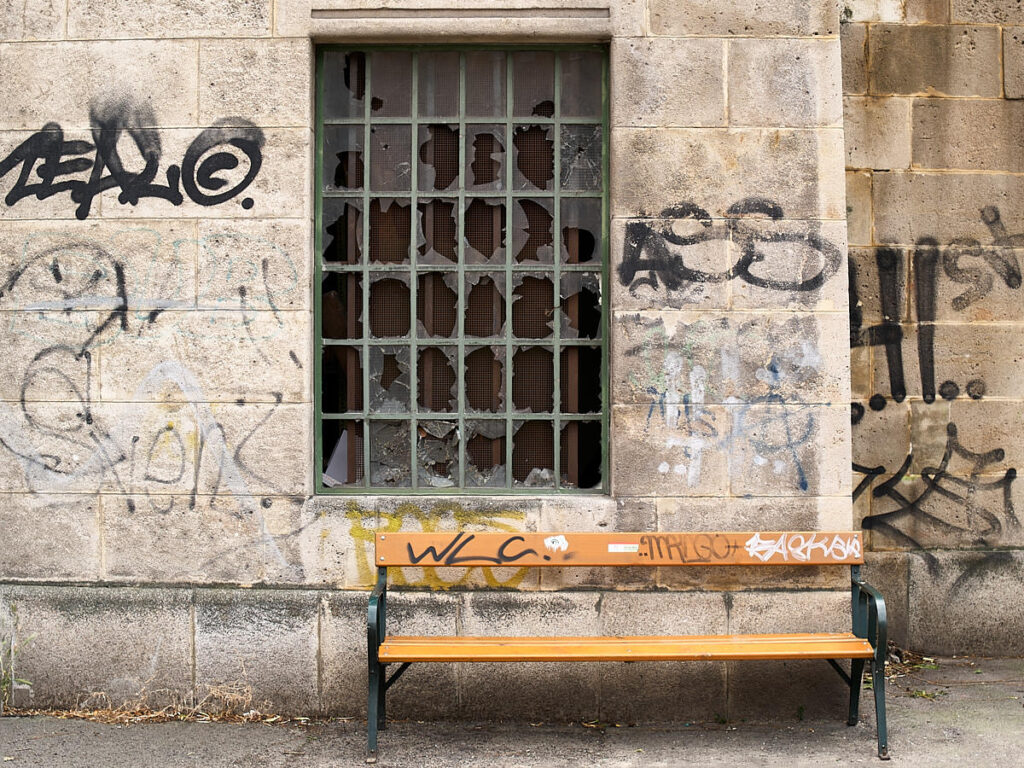Eine Sitzbank vor einem devastierten Gebäude mit eingeschlagenem Fenster