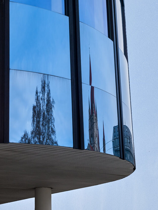 Die Spiegelung eines Kirchturms an einer gewölbten Glasfront