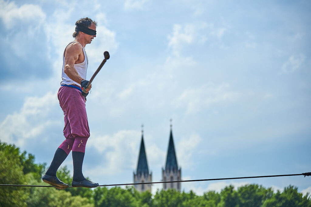 Ein Mann mit Augenbinde unt Balancestange auf einem Drahtseil