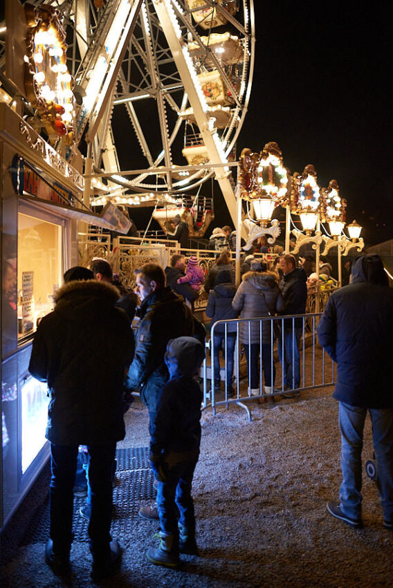 Einige Menschen stehen bei einem Markstand beim Riesenrad.