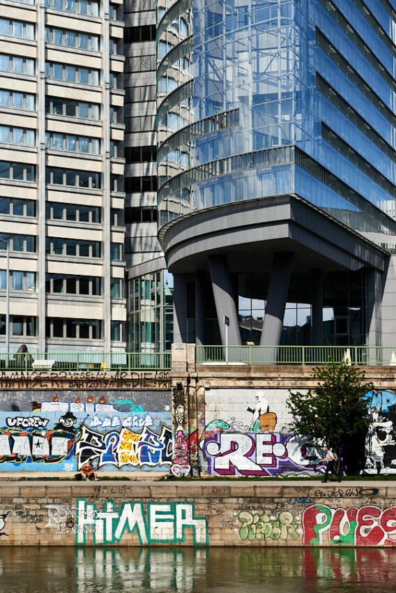 Ein Gebäude auf Stahlstelzen, davon Graffiti an der Uferwand des Donaukanals