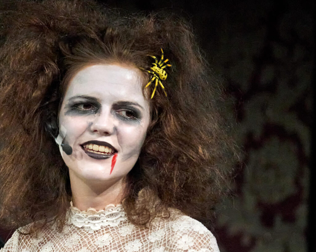 Eine Schauspielerin im Vampirkostüm mit gelber Spinne im Haar
