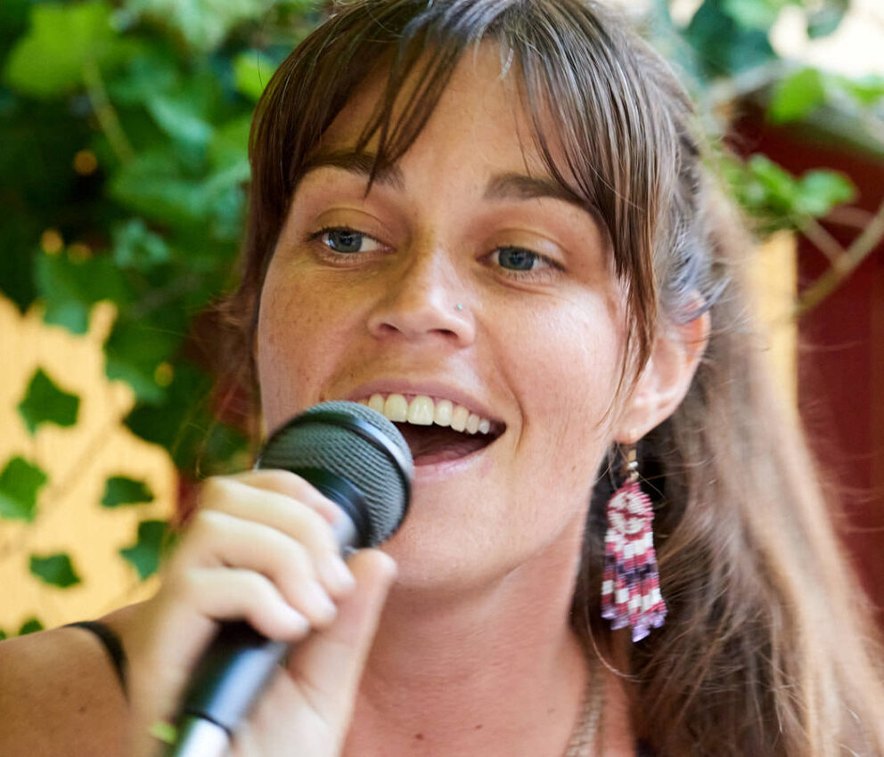 Eine Musikerin mit sonnigem Gesichtsausdruck und einem Mikrofon in der Hand