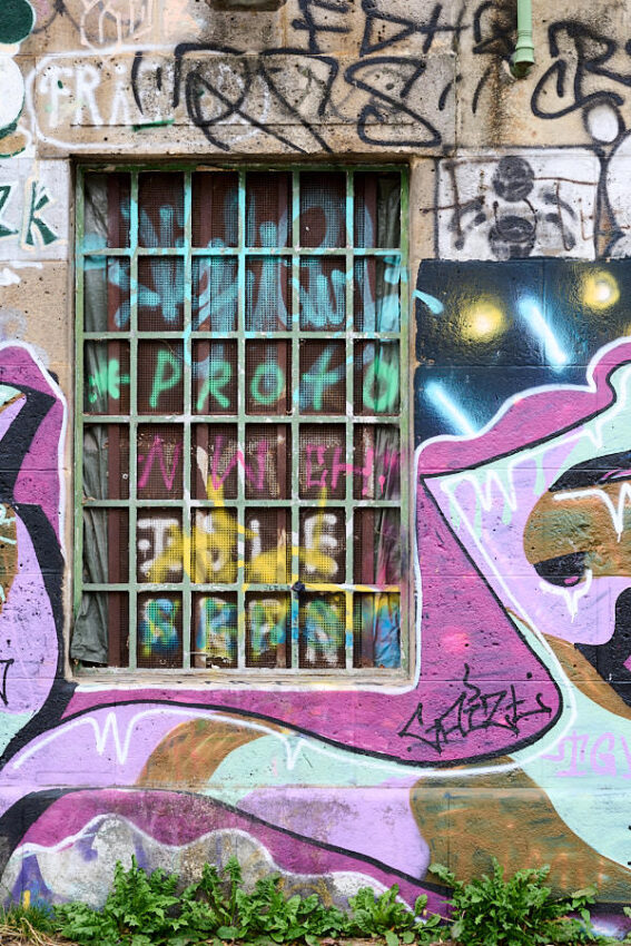 Ein bemaltes Gitterfenster, umgeben von Graffiti