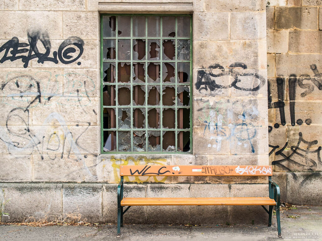 Bank vor Steinfassade mit zerschlagenem, vergittertem Fenster