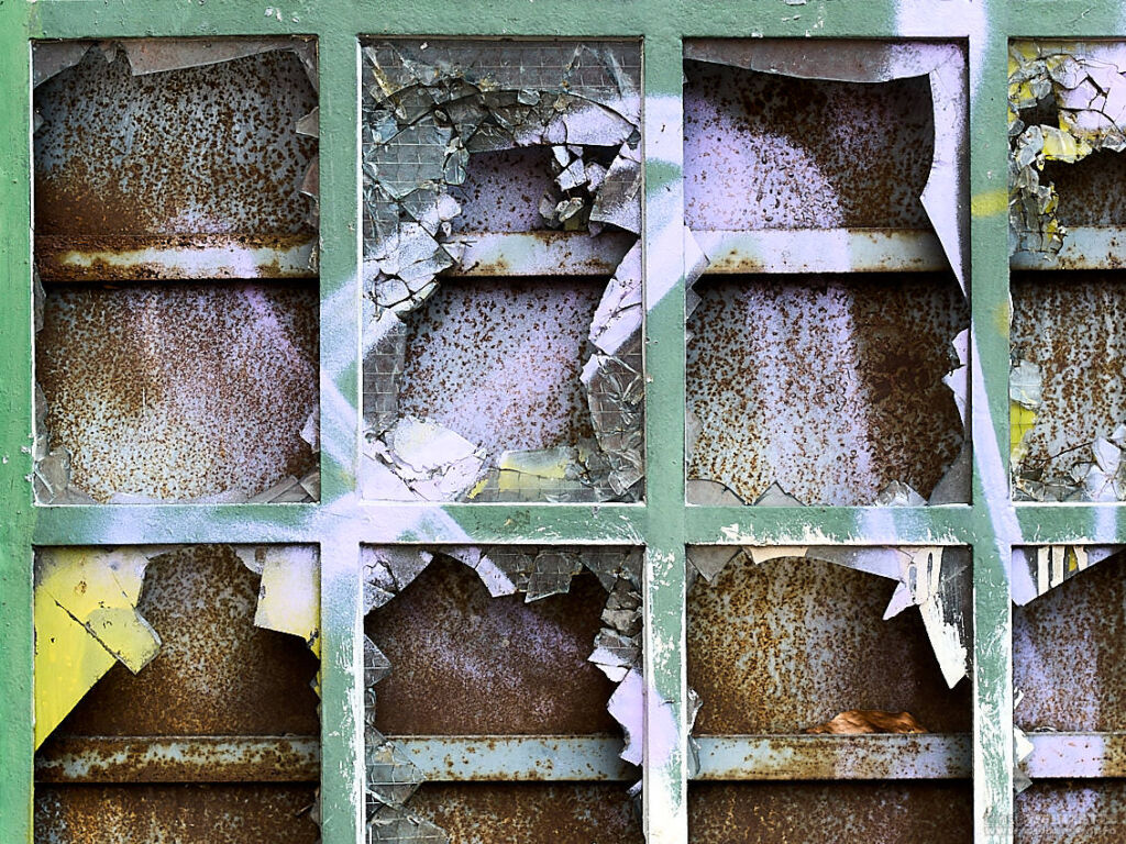 Vergittertes, eingeschlagenes und mit Graffiti bemaltes Fenster